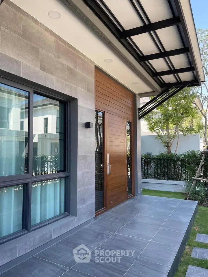 Modern house exterior with sleek design and large windows, featuring a stylish entrance and lush greenery.