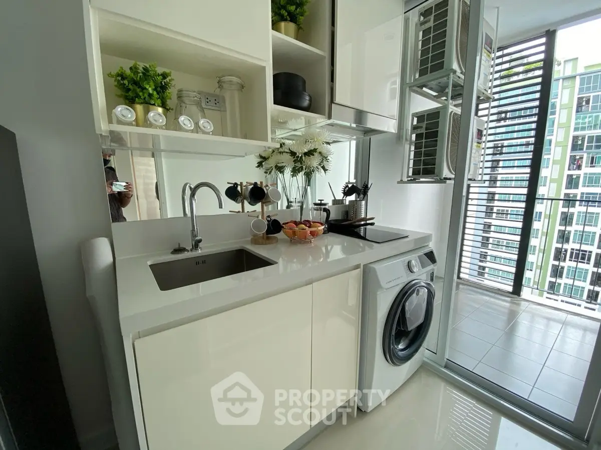 Modern kitchen with sleek cabinetry and integrated washing machine, featuring a bright balcony view.