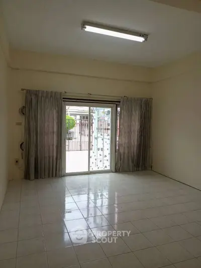 Spacious living room with sliding glass doors leading to a patio, featuring tiled flooring and neutral curtains.