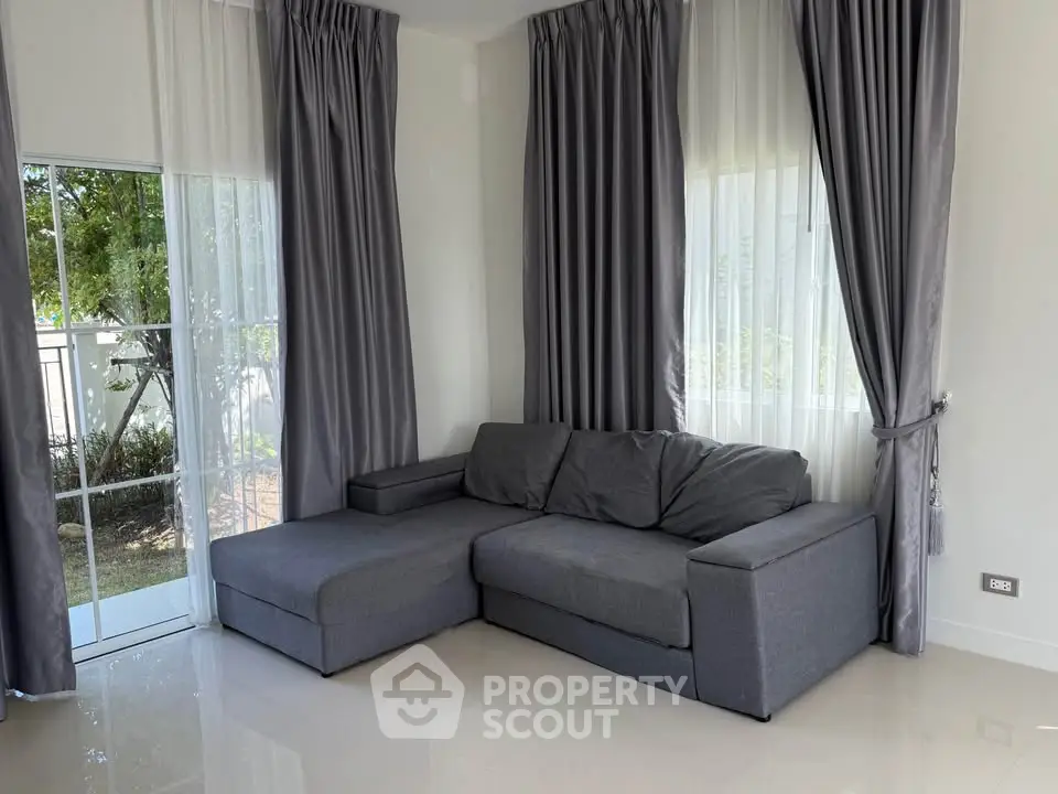 Modern living room with sleek gray sofa and elegant floor-to-ceiling curtains, offering a serene garden view.