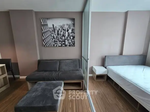 Modern studio apartment with sleek furniture and cityscape artwork, featuring a cozy living area and comfortable bed.