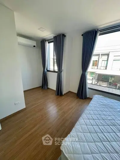 Bright bedroom with large windows and modern curtains, featuring a comfortable bed and wooden flooring.