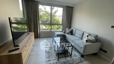 Spacious and modern living room with large windows offering ample natural light, featuring a comfortable grey sofa, stylish glass coffee table, and sleek entertainment unit.