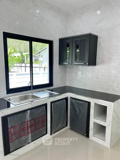 Modern kitchen with sleek black cabinets and large window offering a bright and airy atmosphere.