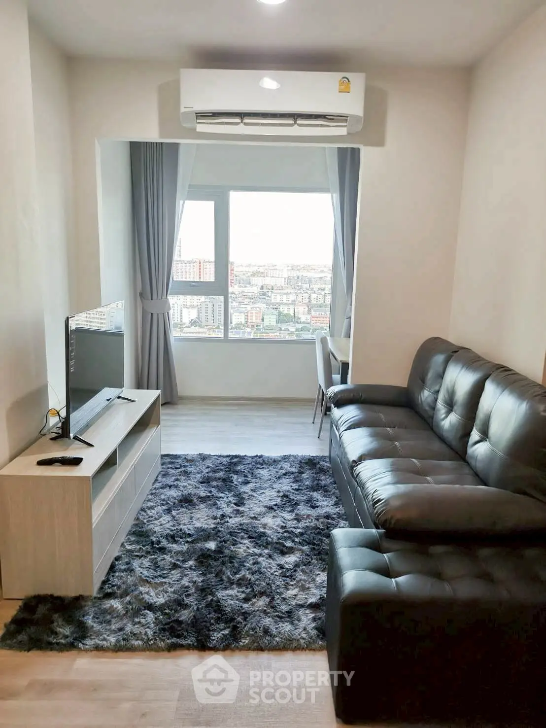 Modern living room with city view, featuring sleek black sofa and stylish entertainment unit.