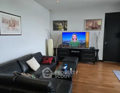 Modern living room with black leather sofa and large TV, featuring stylish decor and wooden flooring.