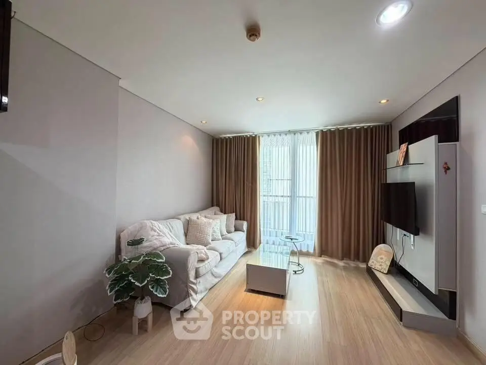 Spacious living room with modern decor and natural light, featuring a cozy sofa and wall-mounted TV.