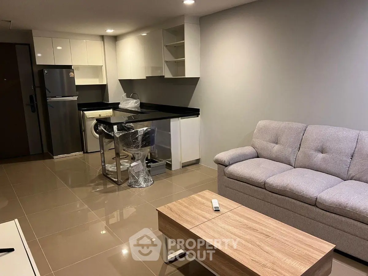 Modern open-layout living room with kitchen, featuring sleek furniture and neutral tones.