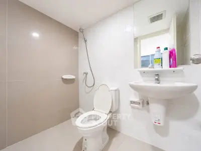 Modern bathroom with sleek fixtures and neutral tiles, featuring a toilet, sink, and shower area.