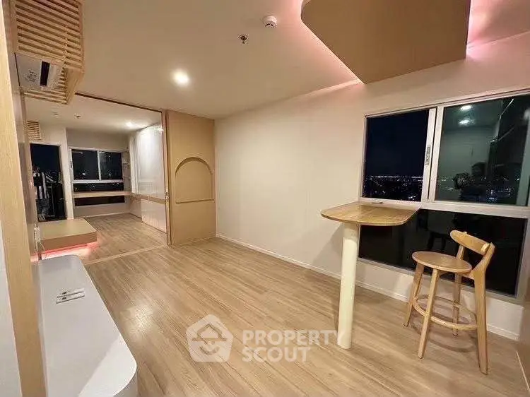 Modern open-plan living room with wooden flooring and city view, featuring stylish furniture and ambient lighting.