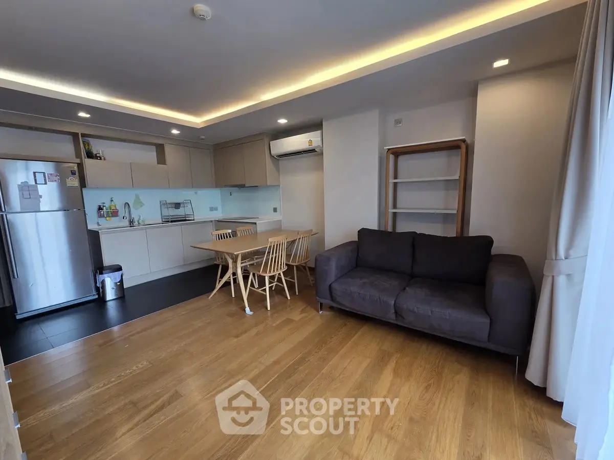 Modern open-layout living room with kitchen, featuring sleek design and wooden flooring.