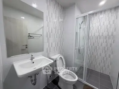 Modern bathroom with sleek design, featuring a shower, toilet, and sink in a bright, tiled space.