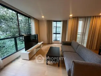 Spacious living room with large windows and modern furniture, offering a serene view of greenery.