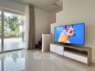 Modern living room with sleek TV setup and large glass doors opening to garden view.