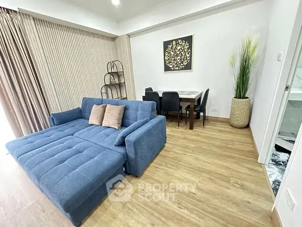 Modern living room with blue sofa and dining area, featuring stylish decor and wooden flooring.
