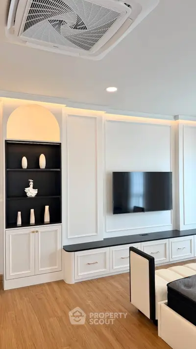 Modern living room with built-in shelving and wall-mounted TV, featuring elegant wood flooring and stylish decor.