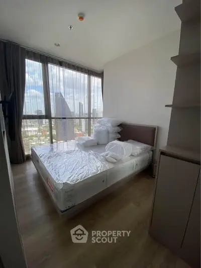 Modern bedroom with large window offering city skyline view, featuring a comfortable bed and stylish decor.