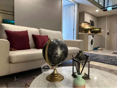 Modern living room with stylish decor and open kitchen layout, featuring a cozy sofa and globe centerpiece.
