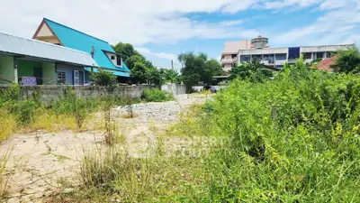 Spacious land plot with lush greenery and nearby residential buildings, perfect for development opportunities.