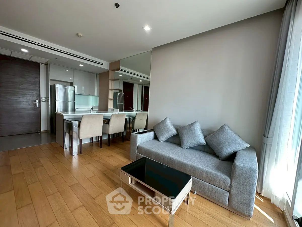 Modern open-layout living room with sleek kitchen and dining area, featuring wooden flooring and stylish furniture.