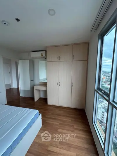 Spacious bedroom with wooden flooring and large window offering city views.