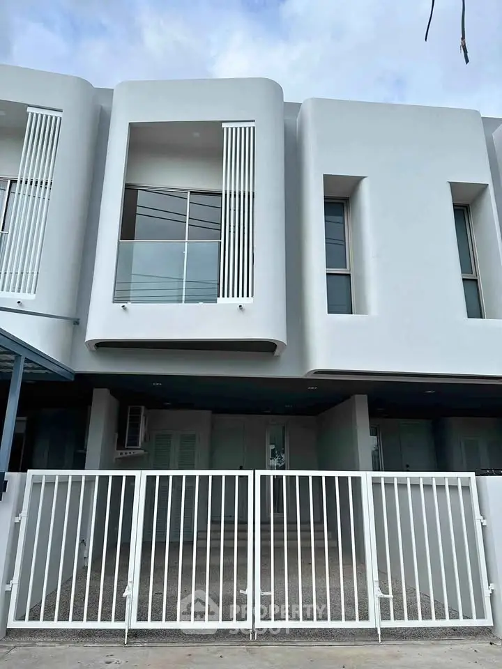 Modern two-story white townhouse with sleek design and gated entrance.