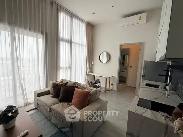 Modern living room with high ceilings, large windows, and open kitchen layout.