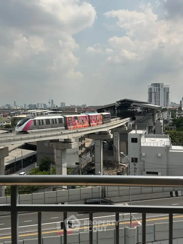 Urban view from balcony overlooking modern train station and city skyline.