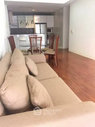 Spacious living room with modern kitchen and wooden flooring in open layout apartment.