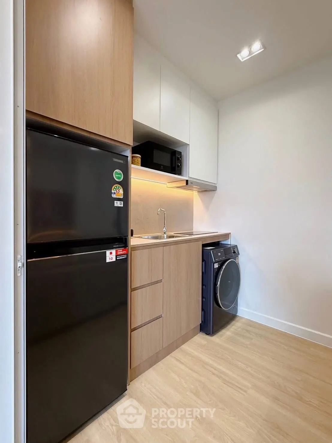 Modern kitchen with sleek appliances and wood cabinetry, featuring a fridge and washing machine.