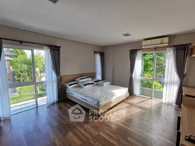 Spacious bedroom with large windows and wooden flooring, offering a serene garden view.