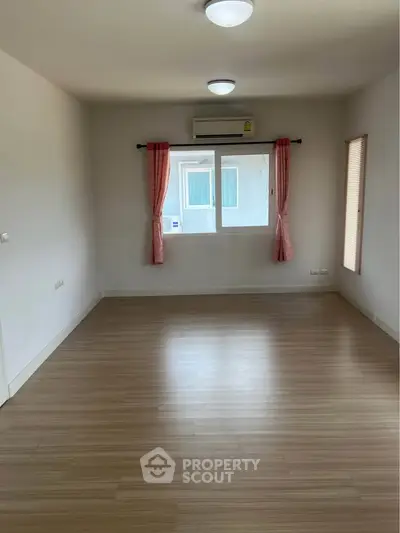Spacious empty room with wooden flooring and large window, perfect for customization.