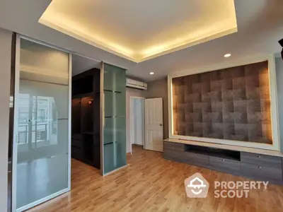 Spacious living room with elegant wooden flooring, modern lighting, and built-in wall units, leading to a glass-enclosed balcony.