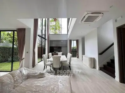 Luxurious modern living room with high ceilings and garden view, featuring elegant dining area and stylish furniture.