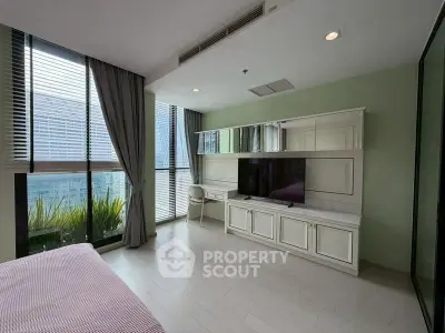 Modern bedroom with large windows and built-in entertainment unit in urban apartment.