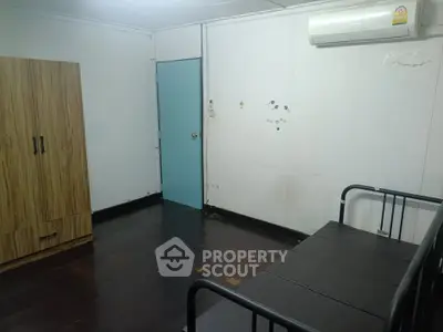 Cozy room with air conditioning and wooden flooring, featuring a wardrobe and a simple bed setup.