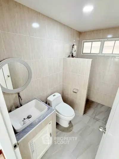 Modern bathroom with sleek fixtures and neutral tiles, featuring a round mirror and compact sink.