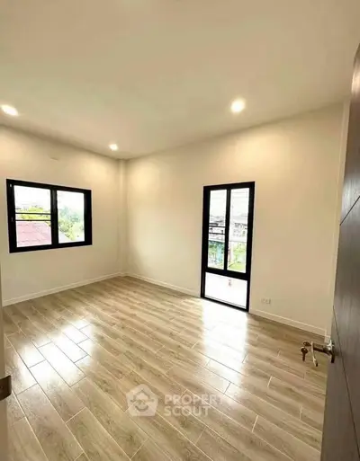 Spacious and bright empty room with wooden flooring and large windows.