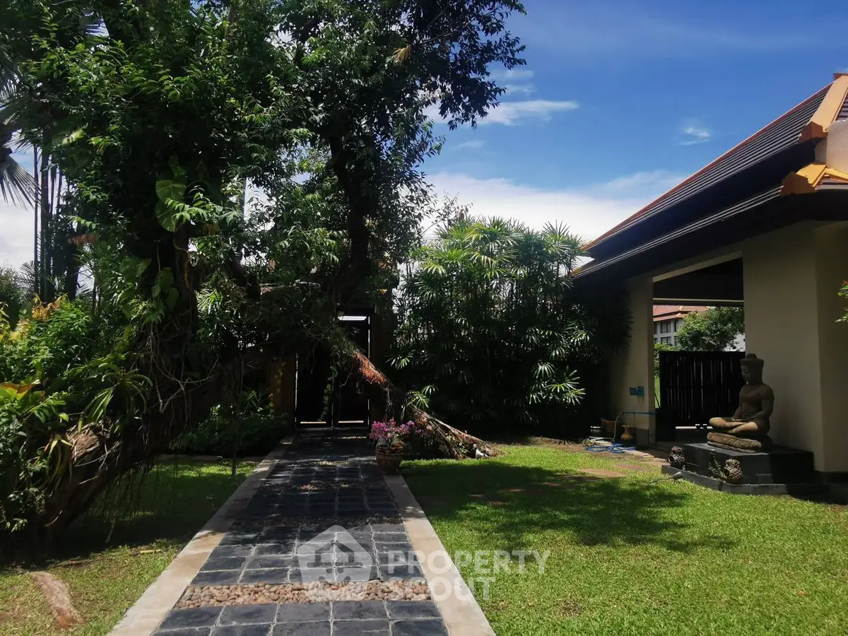 Serene garden with Buddha statue and lush greenery under a clear blue sky.