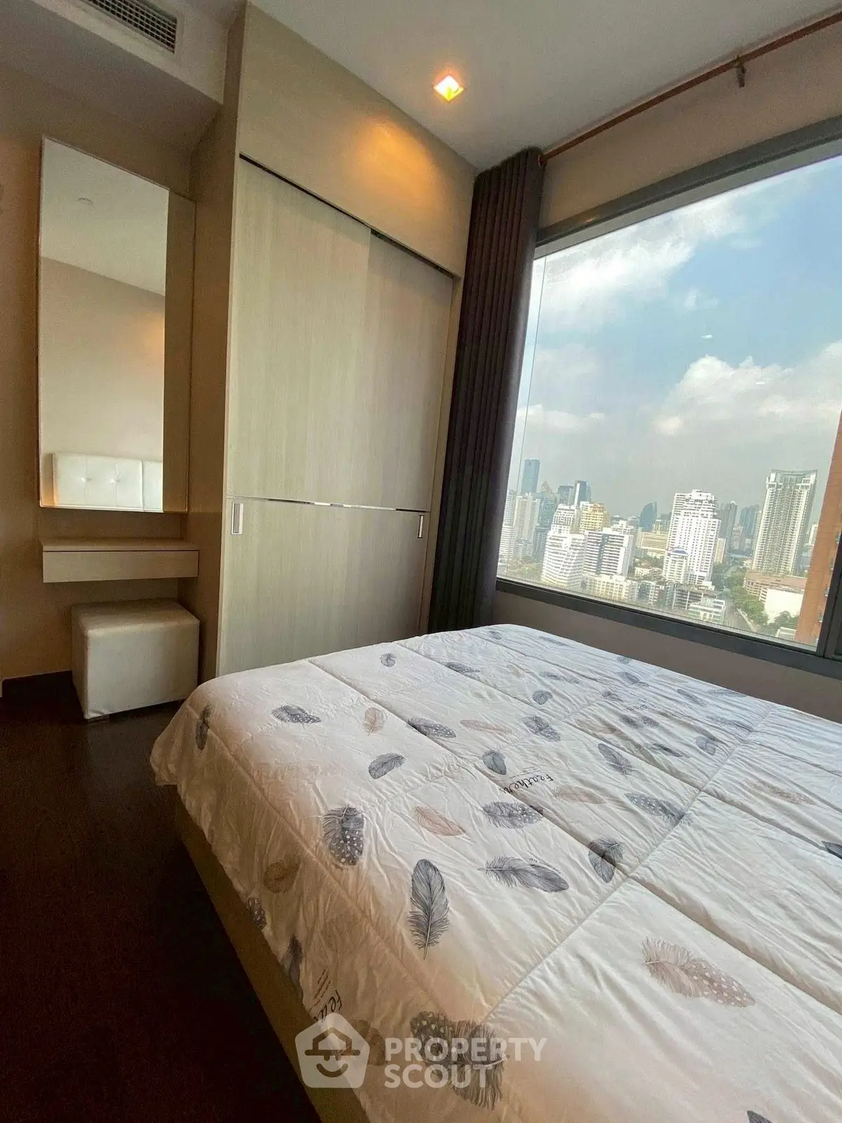 Spacious bedroom with large window offering stunning city views in modern apartment.