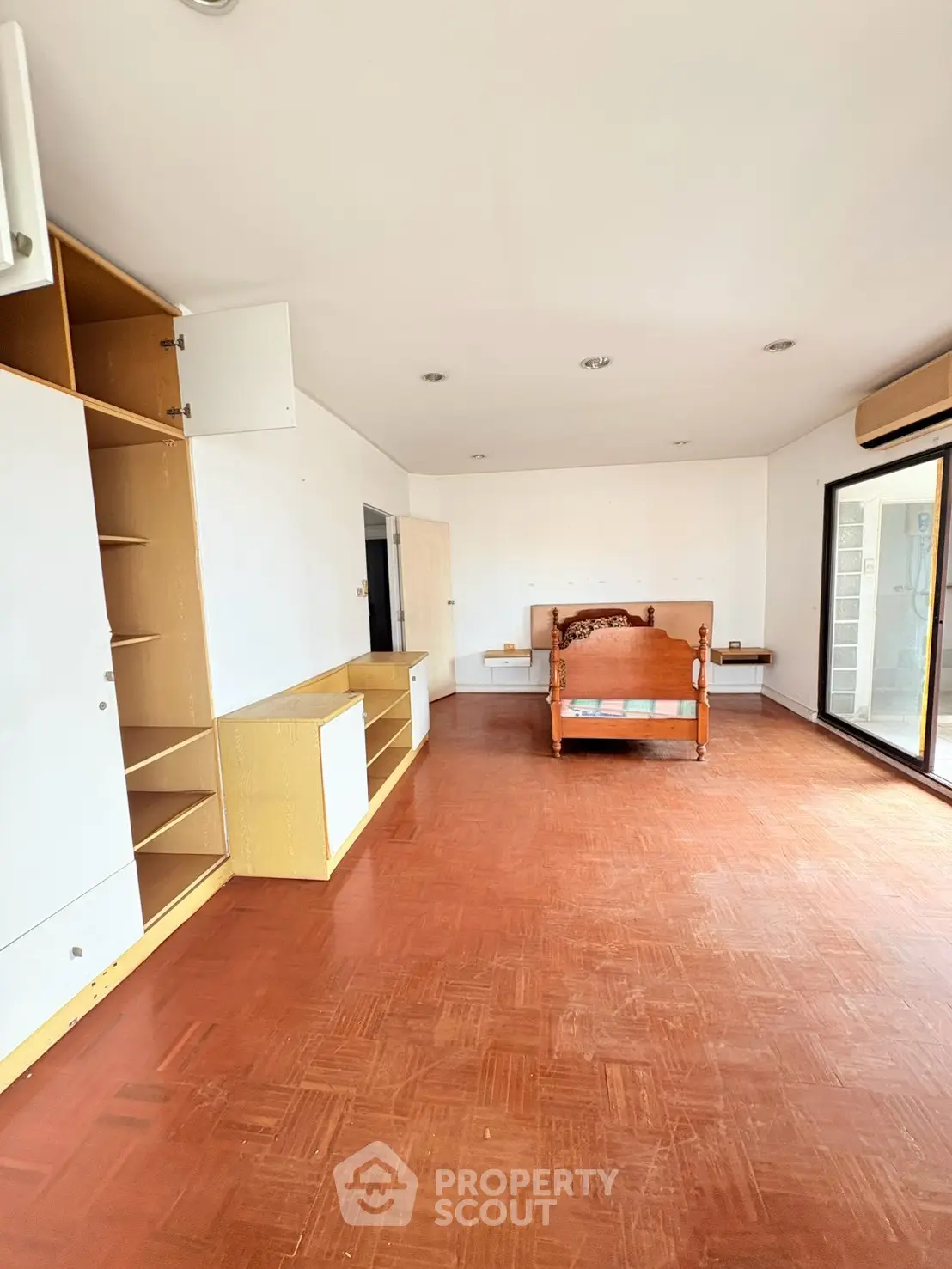 Spacious living room with wooden flooring and built-in storage, featuring a large window for natural light.