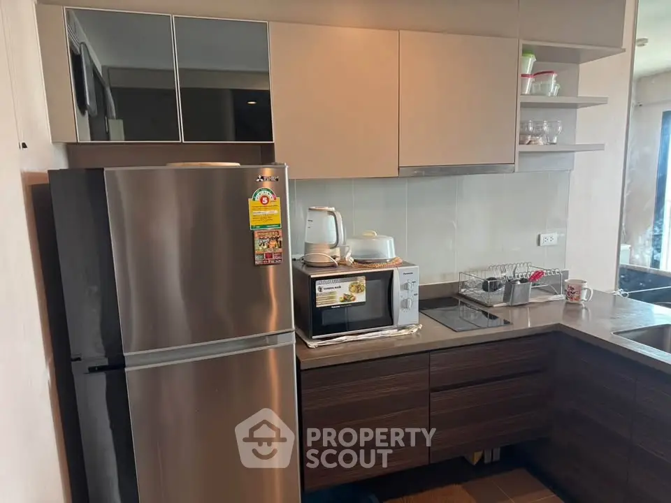 Modern kitchen with sleek cabinets, stainless steel fridge, and built-in microwave in a cozy apartment.