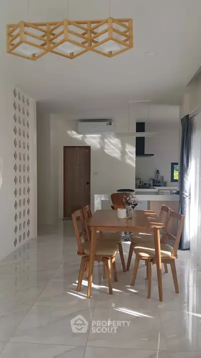 Modern dining area with wooden furniture and open kitchen layout in bright, sunlit room.
