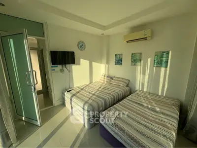 Cozy bedroom with twin beds, wall-mounted TV, and air conditioning in a sunlit room.