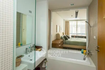 Modern bathroom with bathtub and view into a cozy bedroom, featuring sleek design and natural light.