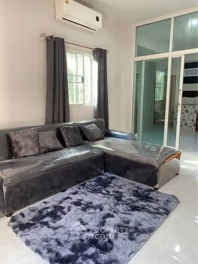 Modern living room with sleek grey sofa, plush rug, and air conditioning, perfect for relaxation.