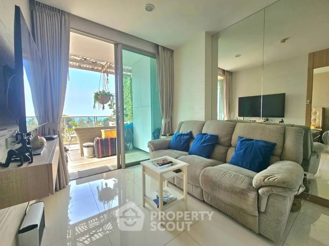 Spacious living room with plush sofa and balcony offering stunning ocean view.