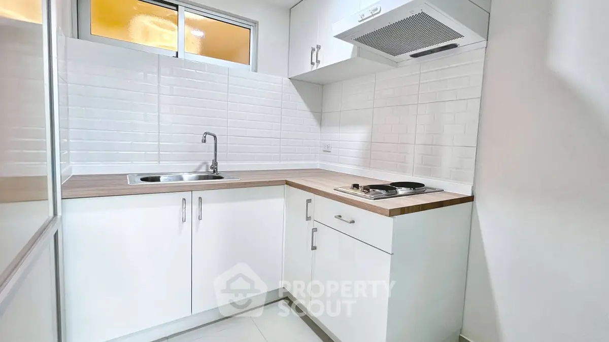 Modern compact kitchen with sleek white cabinets and electric cooktop