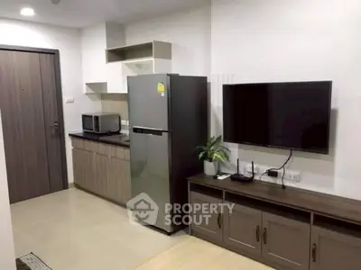 Modern apartment interior with sleek kitchen and living area featuring a stainless steel fridge and wall-mounted TV.