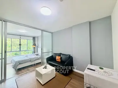 Modern studio apartment with cozy living area and bedroom separated by glass partition, featuring natural light.